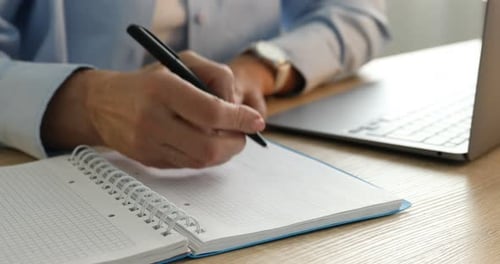 Hands Write in Notebook Next to Laptop