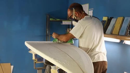 Man Shaping Surfboard in a Workshop