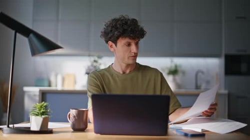 Man Works at Laptop Reviewing Documents at Home
