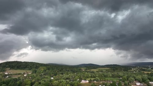 A rising aerial view of a big rainstorm moving over the countryside.