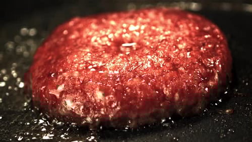 Juicy burger patty sizzles in a hot pan
