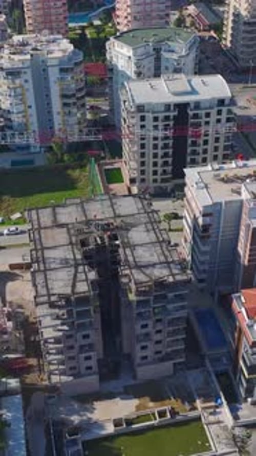 Vertical Video of Workers Pouring Concrete and Erecting Walls While a Crane Assists on Site
