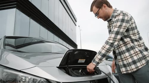 Man Charging Electric Car and Using Phone