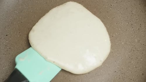 I turn the pancake over in a frying pan with a silicone spatula. view from above. Slow motion