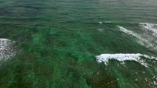 Aerial Top Down View of Beautiful Emerald Ocean Waves Breaking Over the Clear Transparent Sea Water