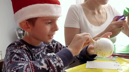 Boy Decorating Christmas Ornament With Family at Home