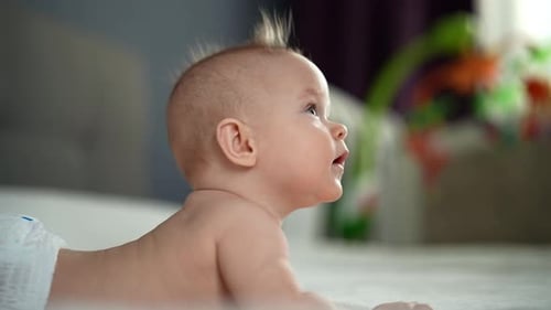 Happy Pretty Active Healthy Newborn Baby Lying in Bed Trying to Crawl Waving Hand at Home Side View