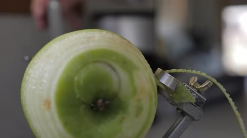 Slow motion front view of green apple being turned and peeled by kitchen device to reveal flesh on b