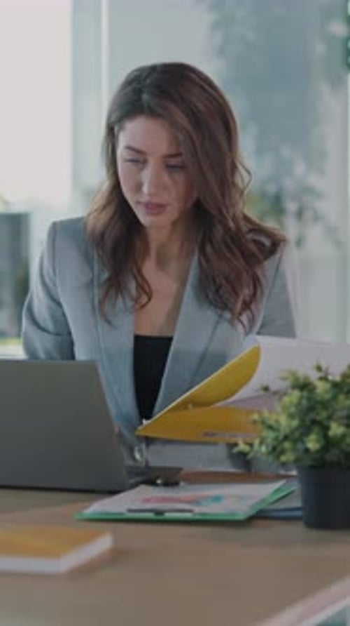 A Professional Woman Works on a Laptop Surrounded By Important Documents in a Modern Office