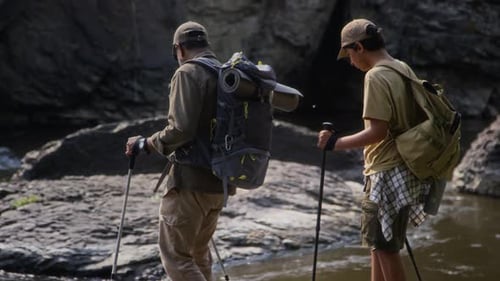 Polyethnic Dad and Son with Backpacks Trekking along Rapid River