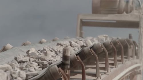 conveyor belt of a stone crusher carrying rocks to be crushed with a sky with clouds in the backgrou