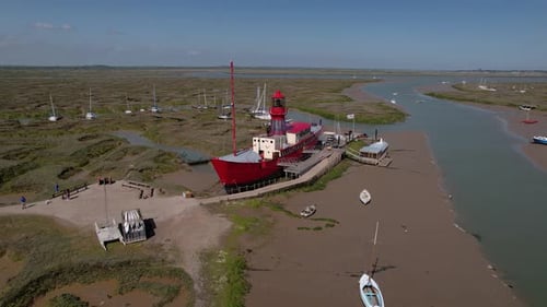 Aerial view orbiting Tollesbury Lightship landmark moored on eroded Essex marina marsh estuary