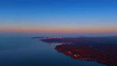 Wooded shore of the sea with residential area. Sunset view of the coastal city from drone.