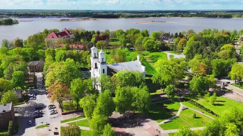 Historic white church surrounded by green park and riverside town – aerial spring view