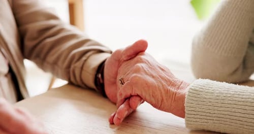Holding hands, love and elderly couple by table for support, sympathy or condolences for loss