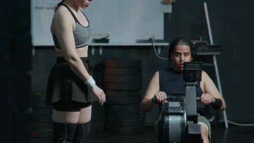 Female Trainer Instructing Young Man in Use of Rowing Machine in Gym