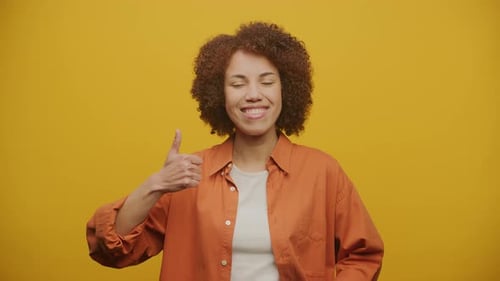 Smiling Woman Gives Thumbs Up on Yellow Background