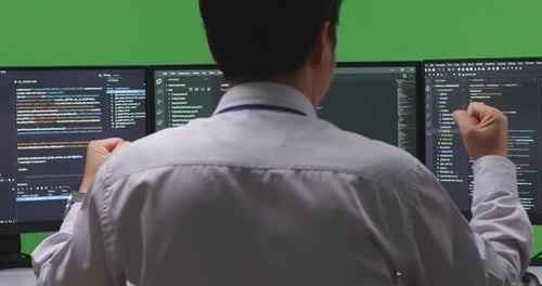 Back View Man Developer Celebrating While Write Code With Multiple Computer Screens In Green Screen