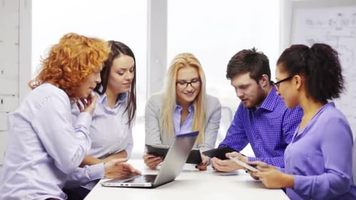 Smiling creative team brainstorming together at modern office table with laptop computers