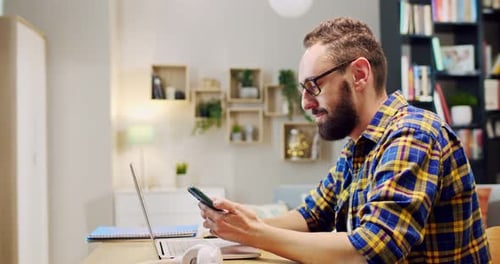 Man Using Laptop and Smartphone at Home