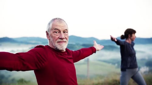 Senior Couple Runners Stretching On Meadow Outdoor In Foggy Morning In Nature.