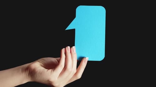 Hand Holding Blue Paper Chat Bubble on Black