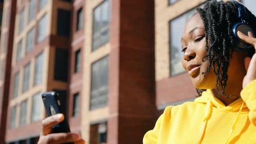 African American Woman Listening to Music with Headphones at Sunset in the City Dancing