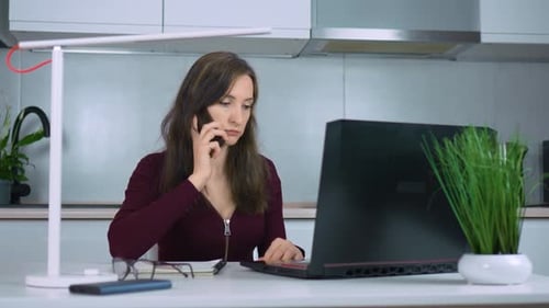 Woman on Phone Working at Laptop at Home
