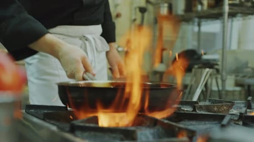 Chef Flipping Food Ingredients in Pan over Fire Flame in Restaurant Kitchen