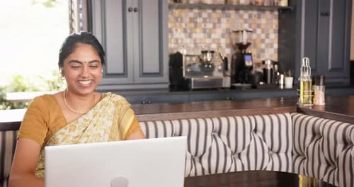 Femme indienne souriante utilisant un ordinateur portable dans la cuisine, travaillant à domicile et appréciant le travail, espace de copie