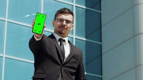 An Office Worker in an Office Suit Raises His Hands with Greenscreen Phone Mockup