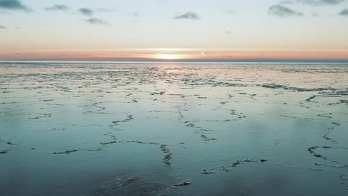 Drone flying over calm sea with melted ice at the surface at sunset, sunrise. Sun low behind the hor