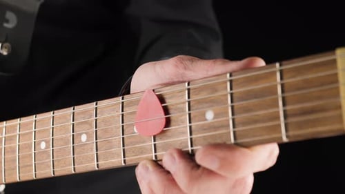 Guitarist take a red pick from the strings of a light brown six-string electric guitar