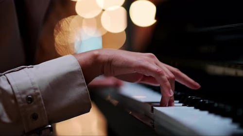 Close up of a woman's hands playing the piano with blurry lights on the background