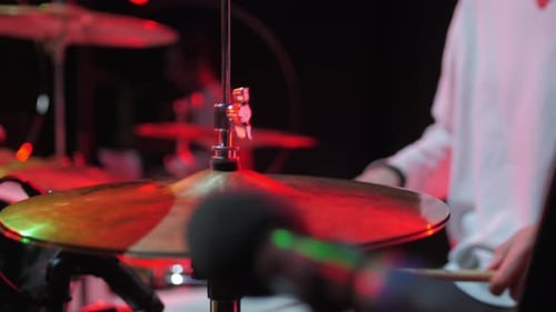 Man Taps Metal Cymbals with Drumsticks Performing on Stage