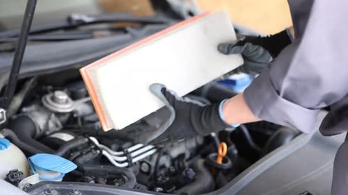 Autoteil. Professioneller Mechaniker mit Luftfilter in der Nähe der offenen Motorhaube des Autos im Innenbereich,
Nahaufnahme
