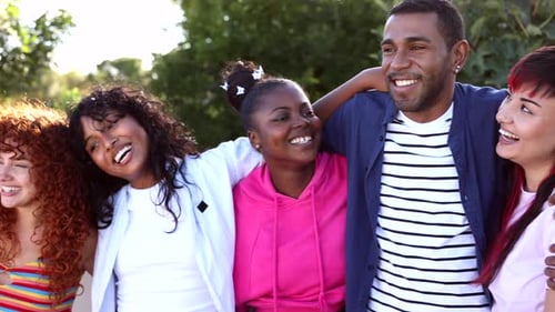 Multiracial lgbt friends sharing warm embrace, laughing together in sunlit park, expressing genuine