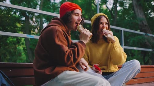 A Couple Enjoys a Casual Moment Sitting Together on a Small Park Bleacher They Share Hot Dogs