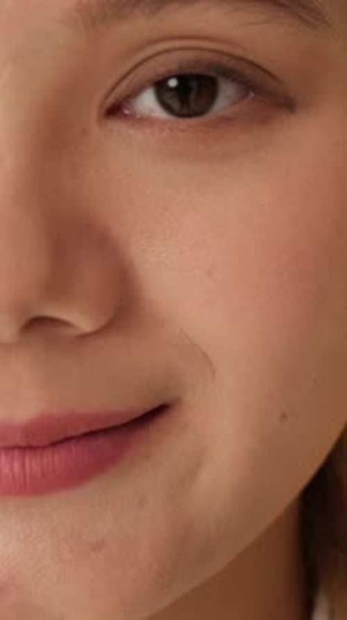 Half face of young woman looking at camera with smile isolated on yellow background in studio
