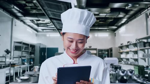 Close Up Of Asian Woman Chef Using A Tablet In Kitchen