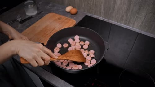 Sausages Sizzling in a Hot Pan Female Hand Stirring with Spatula Closeup Cooking