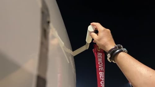 Hand eines Piloten, der vor dem ersten Flug des Tages das rote Etikett „Vor dem Flug entfernen“ entfernt.