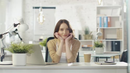 Portrait Shot of a Beautiful Young Girl Sitting at Her Desk in a Brightly Lit Office. She SmilesCh