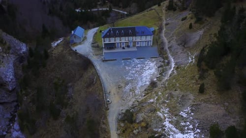 Drone shot of a refuge like building in the middle of a valley in the mountains during the day. Few