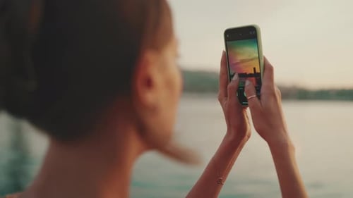 Close-up, girl stands on the embankment and takes pictures of sunrise on a mobile phone