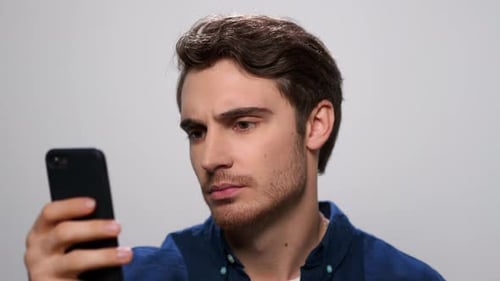 Close Up Upset Man Reading Bad News On Smartphone. Portrait Of Sad Guy Using Phone In Studio. Mal...