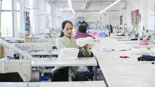Femme couturière assise et comptant des morceaux de tissu en usine