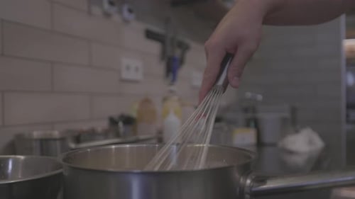 Hand Whisking Liquid in Pot in Kitchen