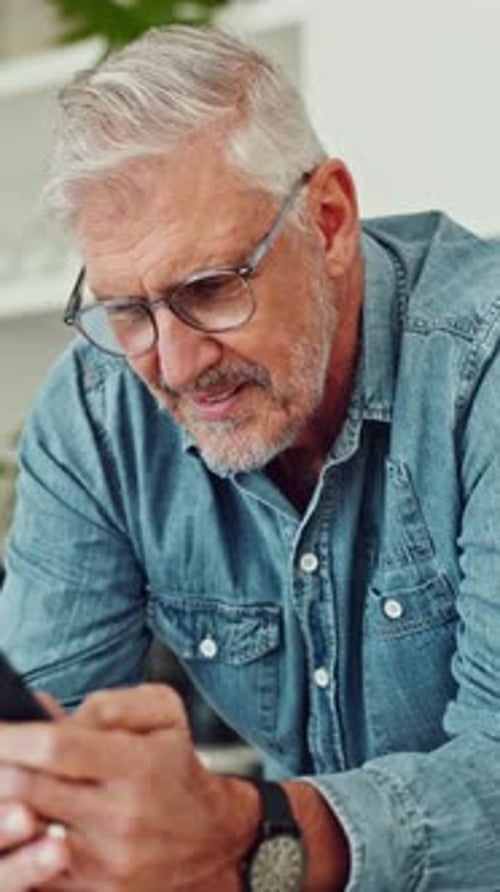 Smiling Man Looking at a Smartphone at Home