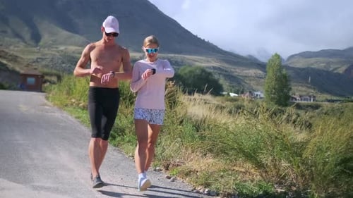 An Athletic Couple Walks a Sunny Road Checking Smartwatches Before Training